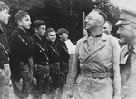 During a visit to the Hochland youth camp, Reichsfuehrer-SS Heinrich Himmler (center) and camp leader Emil Klein (right, in profile) review a group of German youth who are standing in formation.