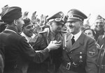A smiling Adolf Hitler greets a soldier.

Pictured at the center with goggles is Hitler's aide-de-camp Heinz Linge.