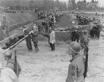 American troops look on as German civilians carry corpses from the grounds of the Nordhausen concentration camp to mass graves for burial.