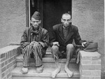 Two emaciated survivors sit outside on the stoop of a barracks in the newly liberated Nordhausen concentration camp.