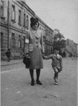 A Jewish mother, wearing an armband, walks along a street with her son in the Krakow ghetto.