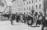 A column of Jews march with bundles down a main street in Krakow during the liquidation of the ghetto.