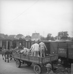 Survivors in uniform transfer corpses from a cart onto a train in preparation for their burial.