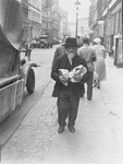 A Jewish man carrying two bags walks down the main commerical street of the Berlin Jewish quarter.