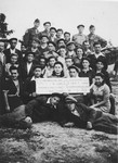 Group portrait of members of the Mizrachi religious Zionist youth movement in the Ziegenhain displaced persons' camp holding a sign that reads, "Our eternity is in Torah, our task is in work."

Two American Jewish soldiers who assisted the group pose with them in the back row.