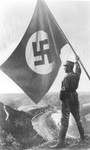 Picture postcard showing a member of the SA waving a large Nazi flag while standing on a mountain ridge overlooking a valley.