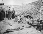 Photographer Francisco Boix and other survivors view a pile of corpses lying among abandoned blankets and clothing in front of a stone wall in the Mauthausen concentration camp.