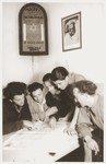 Members of the Kibbutz Nili hachshara (Zionist collective) in Pleikershof, Germany, study a map of Palestine beneath a wall plaque memorializing the six million killed in the Holocaust and a photograph of labor Zionist leader, Berl Katznelson.