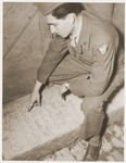 An American serviceman who is visiting the Kibbutz Nili hachshara (Zionist collective) in Pleikershof, Germany, reads a desecrated tombstone that had been used by Julius Streicher for a threshold to a building on his estate.