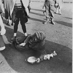 A survivor in Bergen-Belsen, who is too weak to stand, lies on the ground holding a soup bowl.