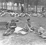 Survivors in Bergen-Belsen peel potatoes while behind them lie the corpses of prisoners who died before the liberation of the camp.