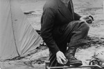 A Bergen-Belsen survivor shines his shoes outside a tent.