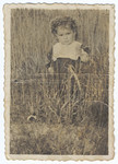 A young Jewish girl in hiding with dyed blond hair walks in a field of tall grass.