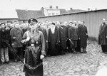 An SS officer stands in front of a line-up of Jewish men in a courtyard or public square in Raciaz.