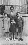 A father and three children stand outside their home on a street in France.