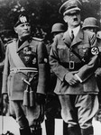 Benito Mussolini and Adolf Hitler stand together on an reviewing stand during a official visit to occupied Yugoslavia.