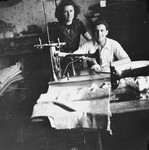 A Jewish woman who is living in hiding as a Christian in a factory in Brussels, poses with a young man who is seated at a sewing machine.