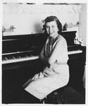 A young Jewish woman poses next to the piano in her home.