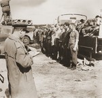 Former camp personnel, including Dr. Fritz Klein, once the camp doctor of Auschwitz and Bergen-Belsen, [third from the right] wait for orders to bury the corpses heaped on the truck behind them.
