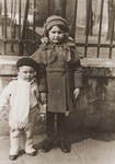 Portrait of two young Jewish children standing outside a park in Warsaw.