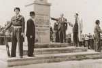 Josef Rosensaft delivers a speech in front of the Bergen-Belsen memorial while DP policeman Nandor Aron stands guard.