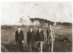 Four young Jewish men wearing yellow stars walk in an open field in the Strzemieszyce ghetto.