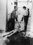 Survivors of the Dachau concentration camp demonstrate the operation of the crematorium by dragging a corpse towards one of the ovens.