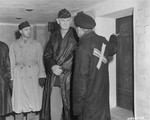 A survivor acting as a guide explains the working of a gas chamber in Dachau to Major General William R.