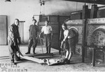 Survivors of the Dachau concentration camp demonstrate the operation of the crematorium by preparing a corpse to be placed into one of the ovens.