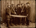 Five young Jewish men who are members of a kibbutz hachshara (Zionist collective) pose holding tools at a logging company in Oczmiana, where they are working to learn the trade and finance their collective.