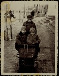 Three young children go for a sled ride on a snowy street in Eisiskes.