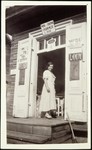 A woman stands by the entrance to a general store.