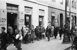 Jews walk along the street in the Warsaw ghetto in front of an ice cream shop.
