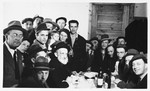 A group of religious Jewish DPs crowd around a table set with food and bottles of wine at the Schlachtensee displaced persons camp.