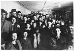 A crowd of Jewish DP men, women, and children attend a meeting or event in a hall in the Schlachtensee displaced persons camp.
