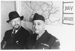 UNRRA camp director Harold Fishbein poses with a civilian in front of a map of Europe in the Schlachtensee displaced persons camp.