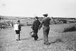 A youth who is living in hiding on a farm in Taluyers, walks through a field with two young men carrying pitchforks.