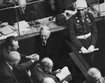 Defendant Hjalmar Schacht, former president of the Reichsbank, talks to his fellow defendants under the eye of an American military police officer at the International Military Tribunal trial of war criminals at Nuremberg.