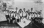 A large group of children from a Zionist youth movement in Dabrowa Gornicza poses in a room decorated with posters and a photograph of Theodore Herzl.