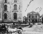 Passengers in a horse-drawn carriage ride through the public square of Drohobycz, past the large synagogue.