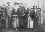 A group portrait of impoverished Jews in Drohobycz standing in front of a stack of lumber.