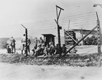 Liberated prisoners gather by the barbed wire fence in front of stacked wood in an unidentified concentration camp.