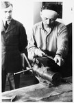 Issak Libstug, wearing his AJDC uniform, watches a religious man filing a piece of metal in a workshop in the Foehrenwald DP camp.