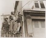 Corporal Calvert Martin and Private Oda Holt help a French boy affix the Tricolor above a Hitler Street sign near the German border.