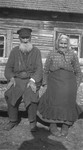 Portrait of an elderly Jewish couple sitting on a log in front of their home in a Lithuanian village.