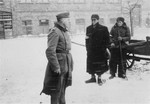A German soldier stands next to two Jewish men who are clearing snow on a street in Czestochowa.