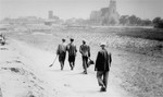 Jewish forced laborers from Belchatow walk along an unpaved road carrying shovels.