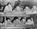 Survivors lie in the top two tiers of a wooden bunk in a barracks in the Buchenwald concentration camp.