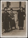 Three religious Jewish men wearing armbands pose on a street in the Bedzin ghetto.
