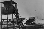 View of a watch tower in front of the burning barracks in camp no.